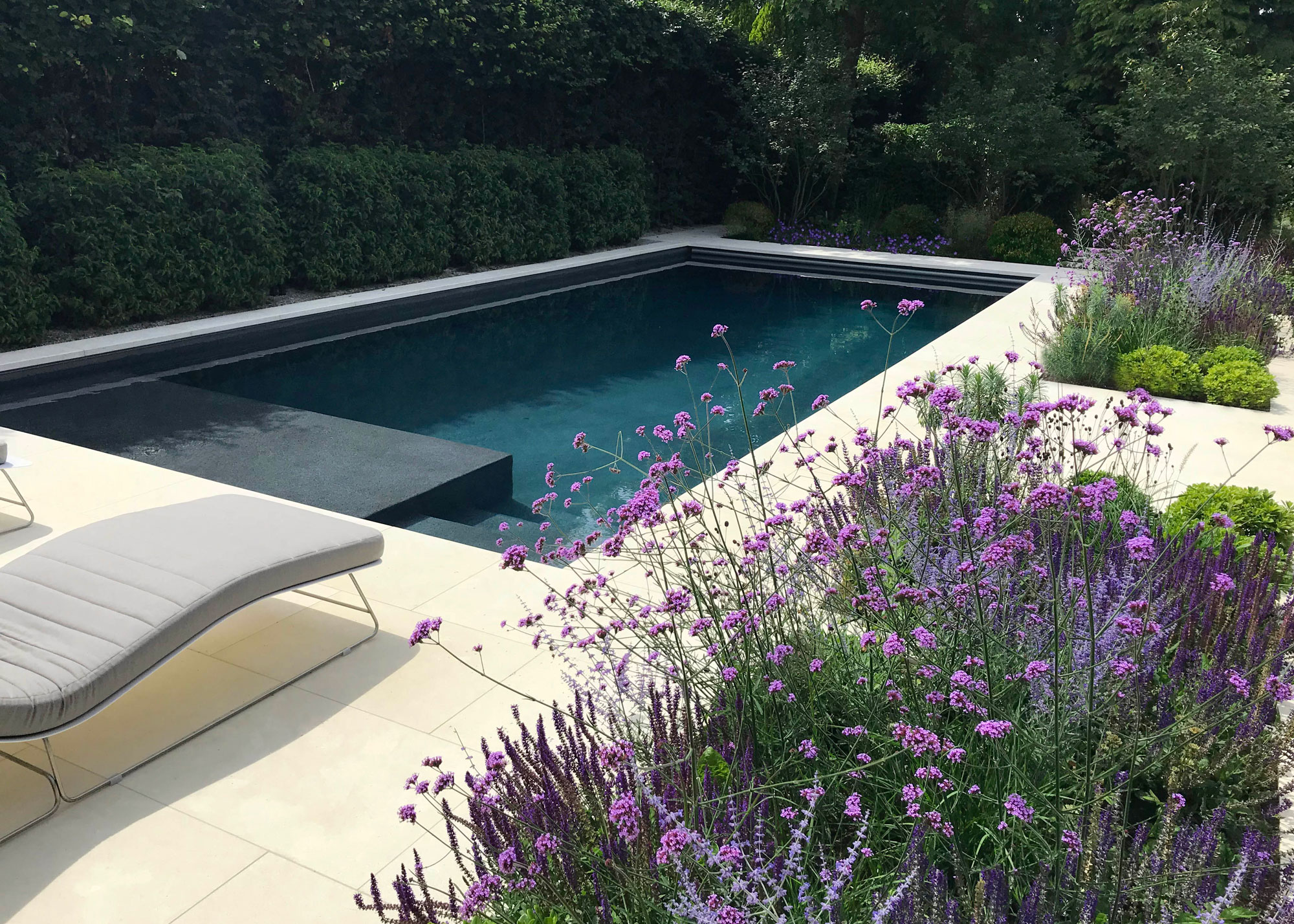 pool patio with sun lounger with planted areas and hedges enclosing the space