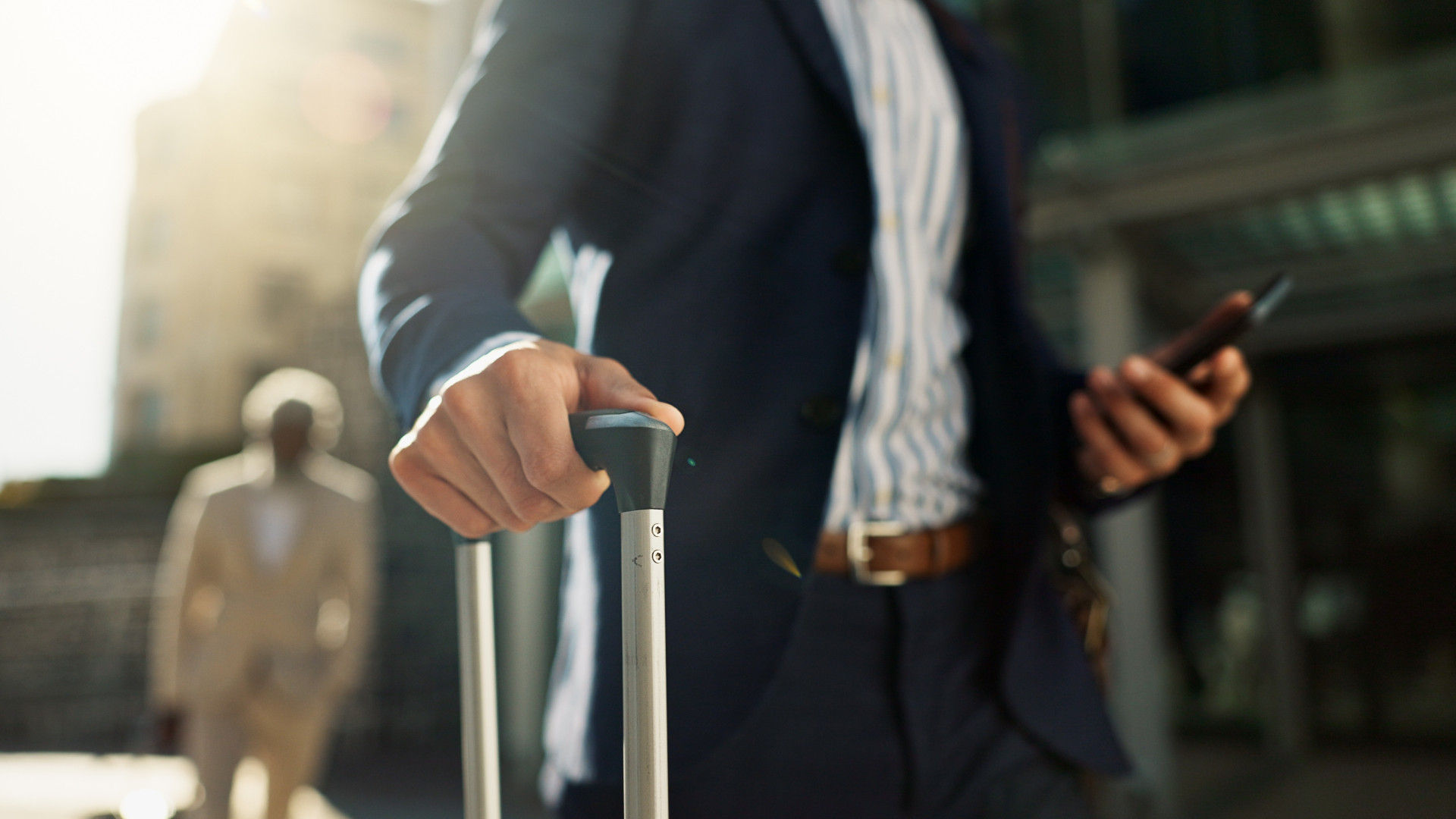 A businessman walking down a street with a suitcase and mobile phone in hand.