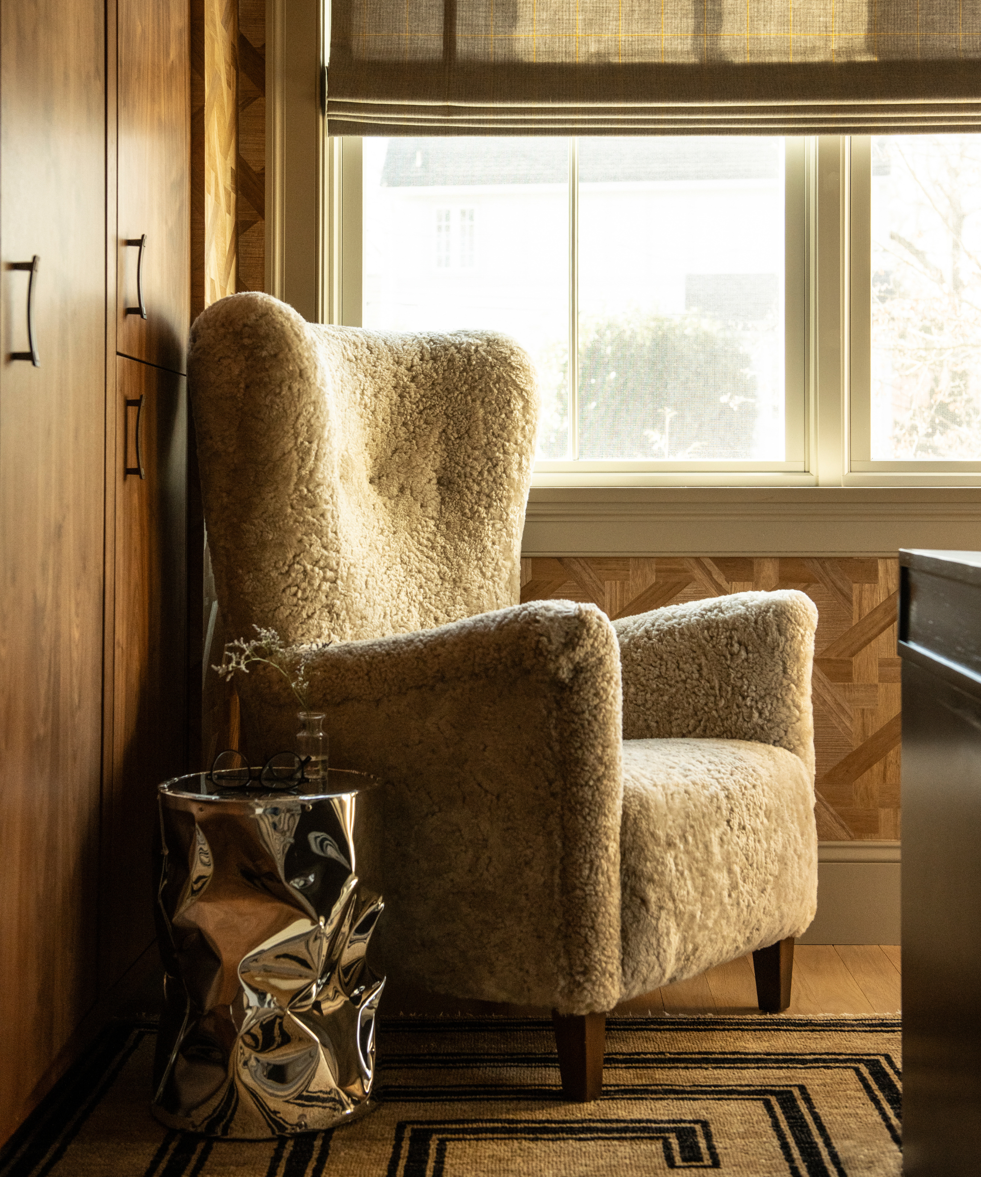 Cozy living room vignette featuring a shearling wingback armchair and a sculptural chrome side table