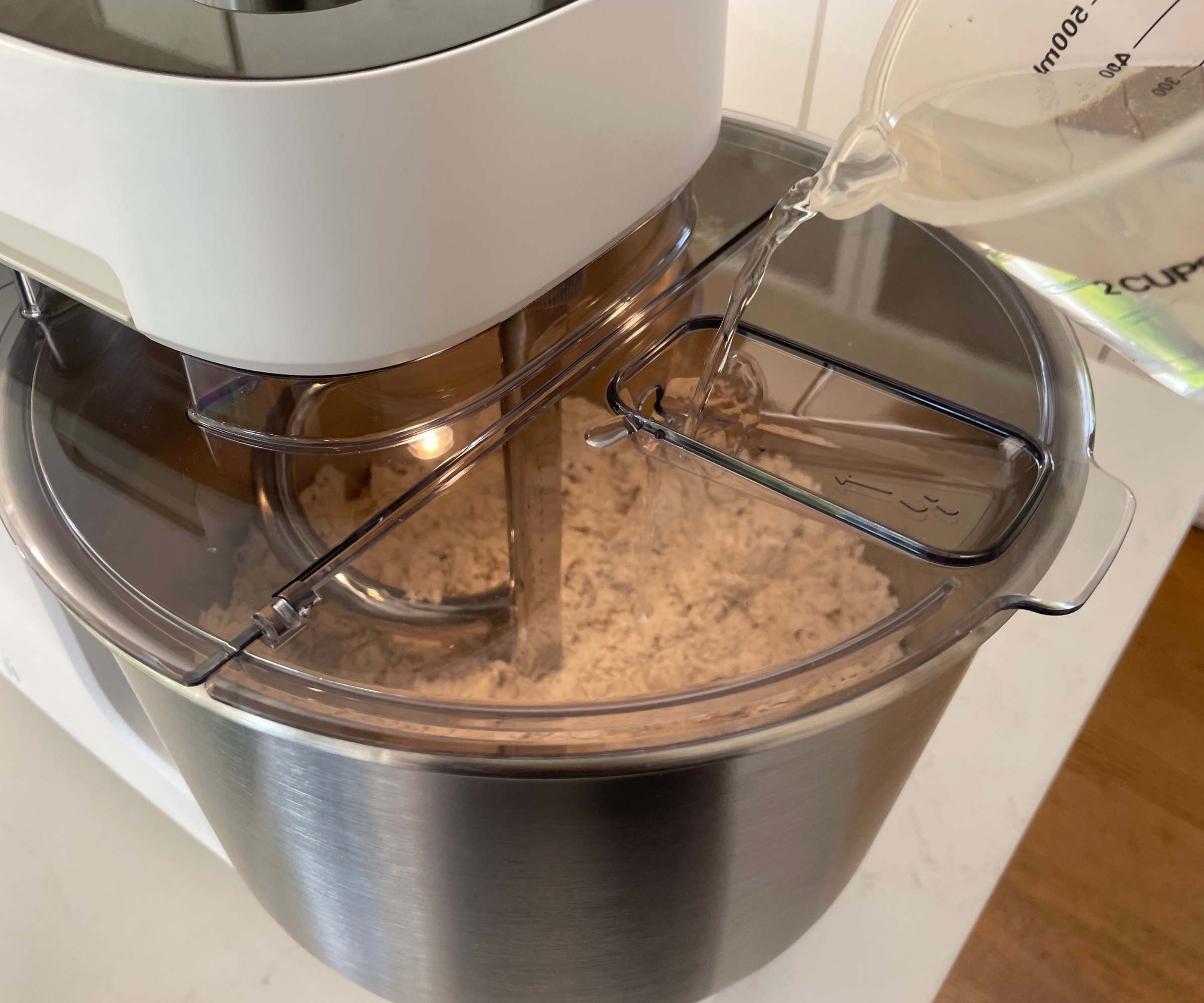 Pouring water into my seeded bread dough mix in the Ooni Halo Pro Spiral Mixer