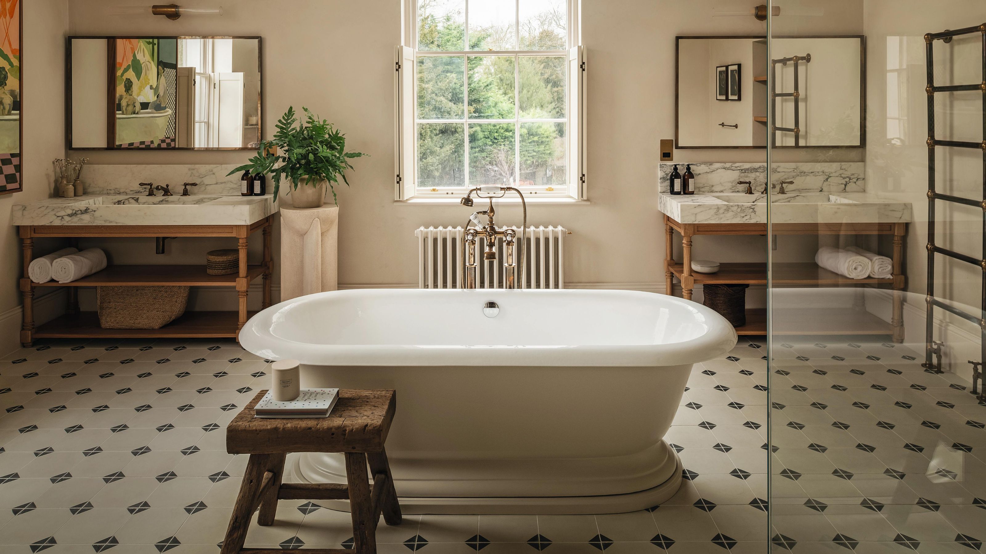 a large victorian bathroom with stone floor, a freestanding tub in the middle of the room, his and hers vanitiies with marble tops and a corner shower
