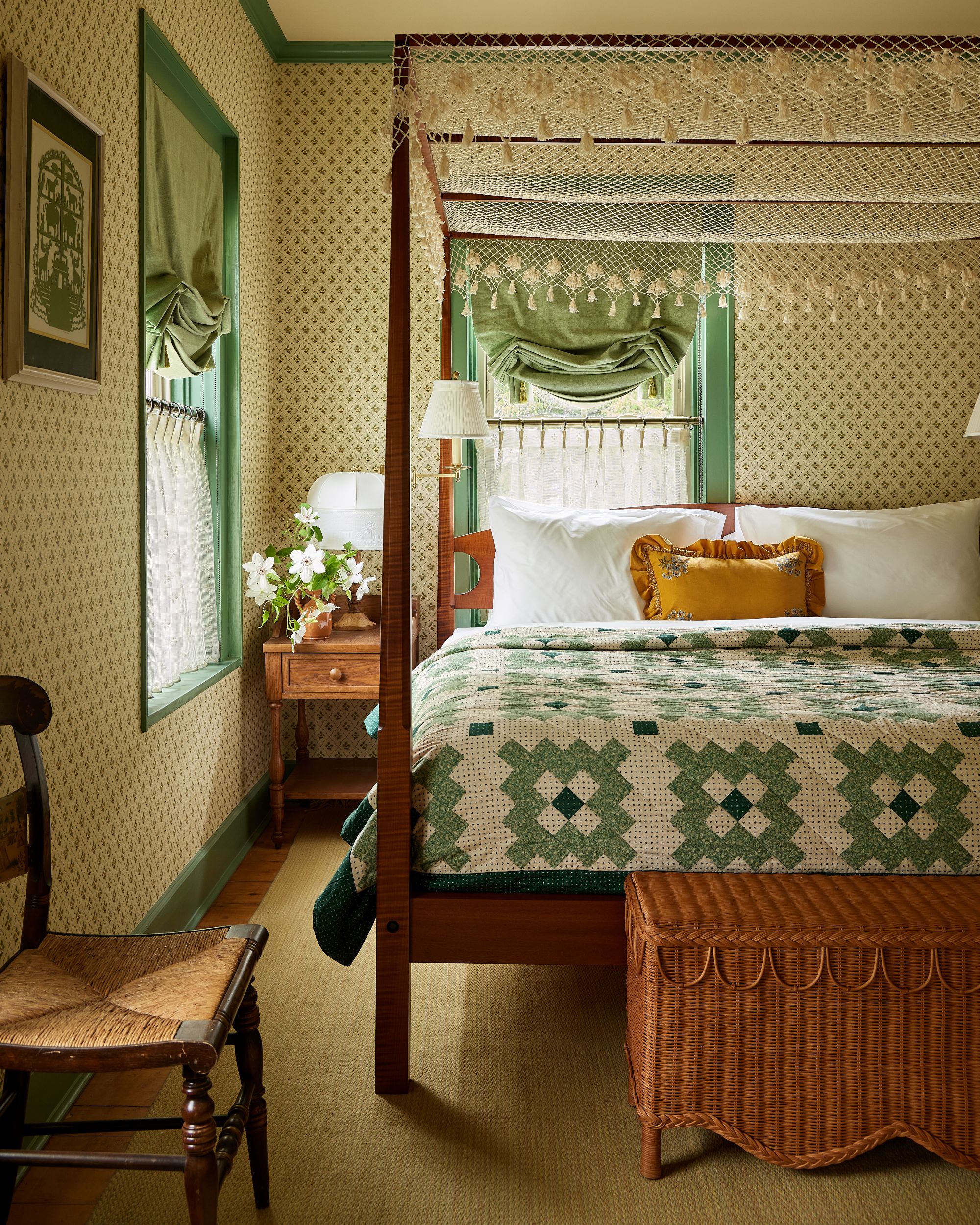 a bedroom with a patchwork bedspread, a dark wood bedframe, a side chair, a wicker basket, and patterned wallpaper on the walls
