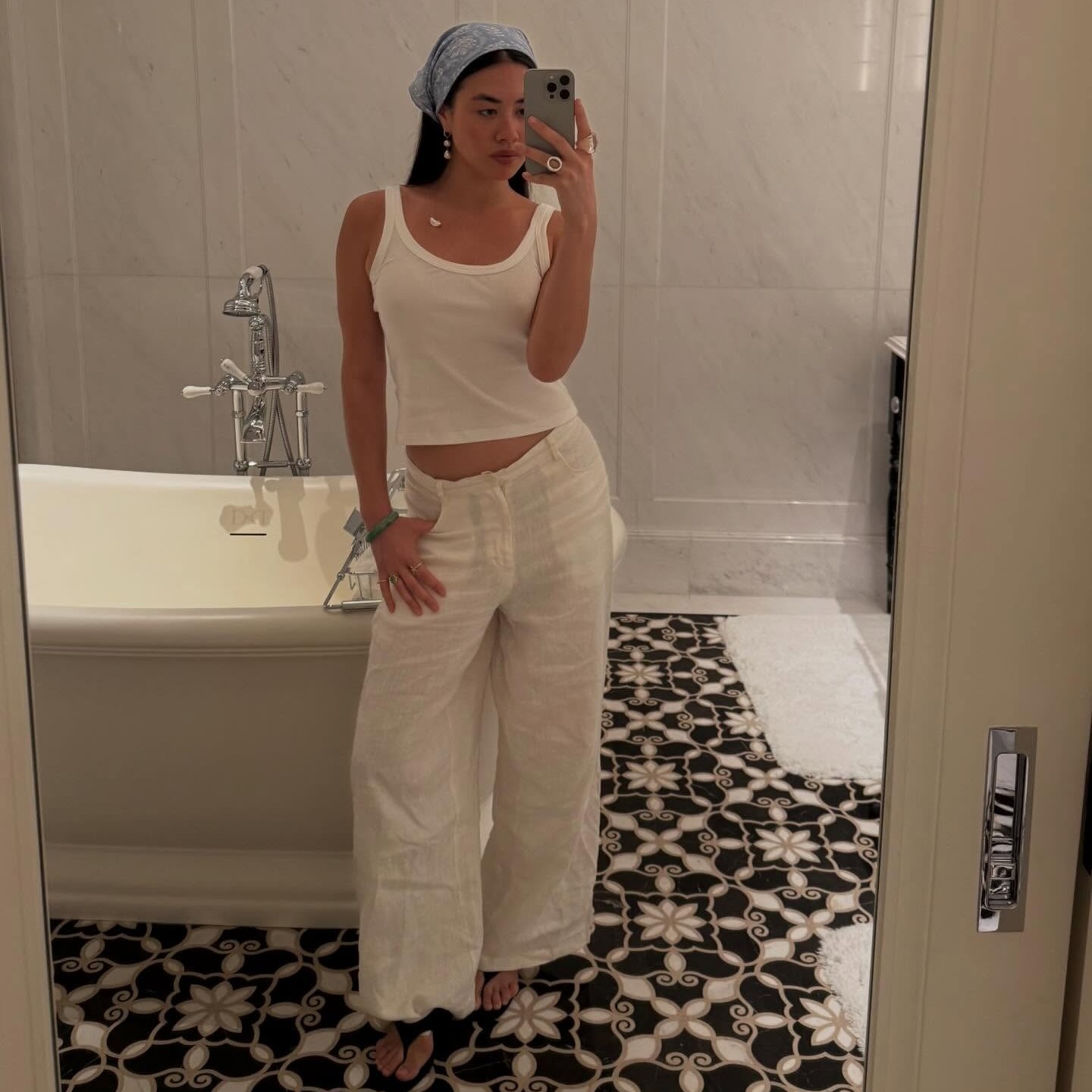 Woman takes a mirror selfie in white cargo pants, white tank top and a head scarf.