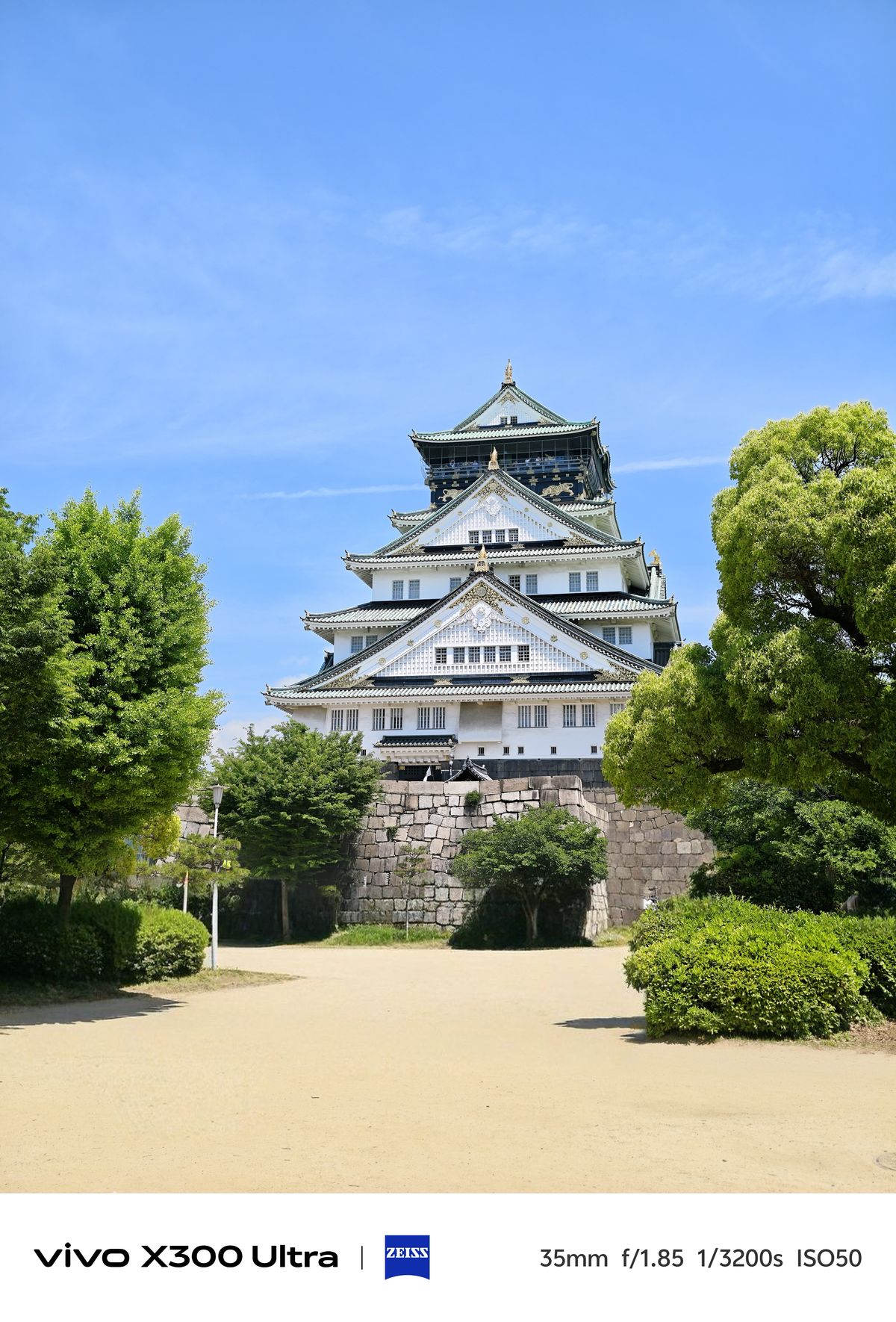 Osaka Castle framed by green trees under a clear blue sky, photographed on the Vivo X300 Ultra.