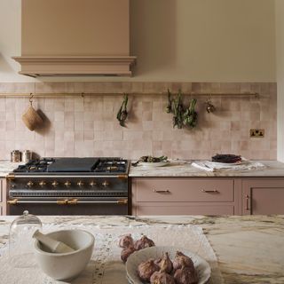 pink cabinetry and extractor fan with black range cooker and subtly pink zellige walls with close up of marble island worktop