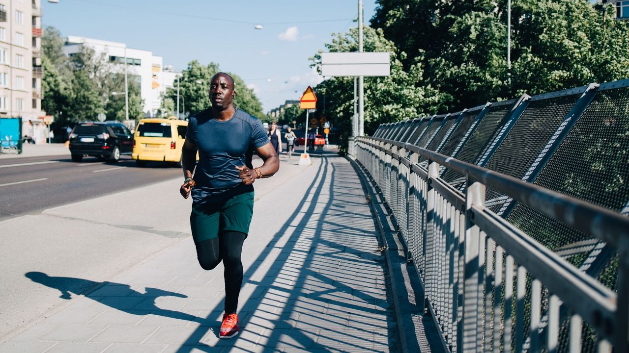 best running tops: pictured here, an athletic man running across a bridge wearing compression leggings, running shorts and a running t-shirt 