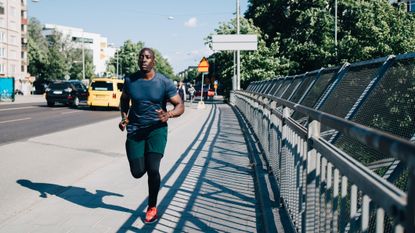 best running tops: pictured here, an athletic man running across a bridge wearing compression leggings, running shorts and a running t-shirt 