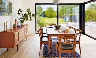 a bright and spacious kitchen extension, with a wooden dining table, a wooden side table to the left with drawers, and floor to ceiling doors with black crittall to the right