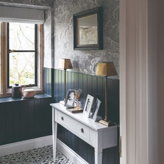 A hallway with half-height vertical wall panelling in navy blue and the upper half with the ceiling covered in a cloudy-print wallpaper