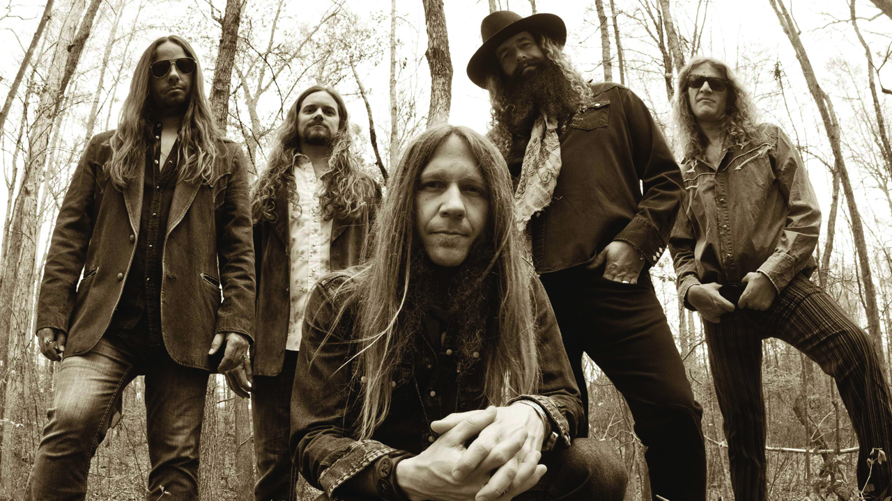 Blackberry Smoke standing in the woods, frontman Charlie Starr kneeling at the front of the group and looking at the camera.