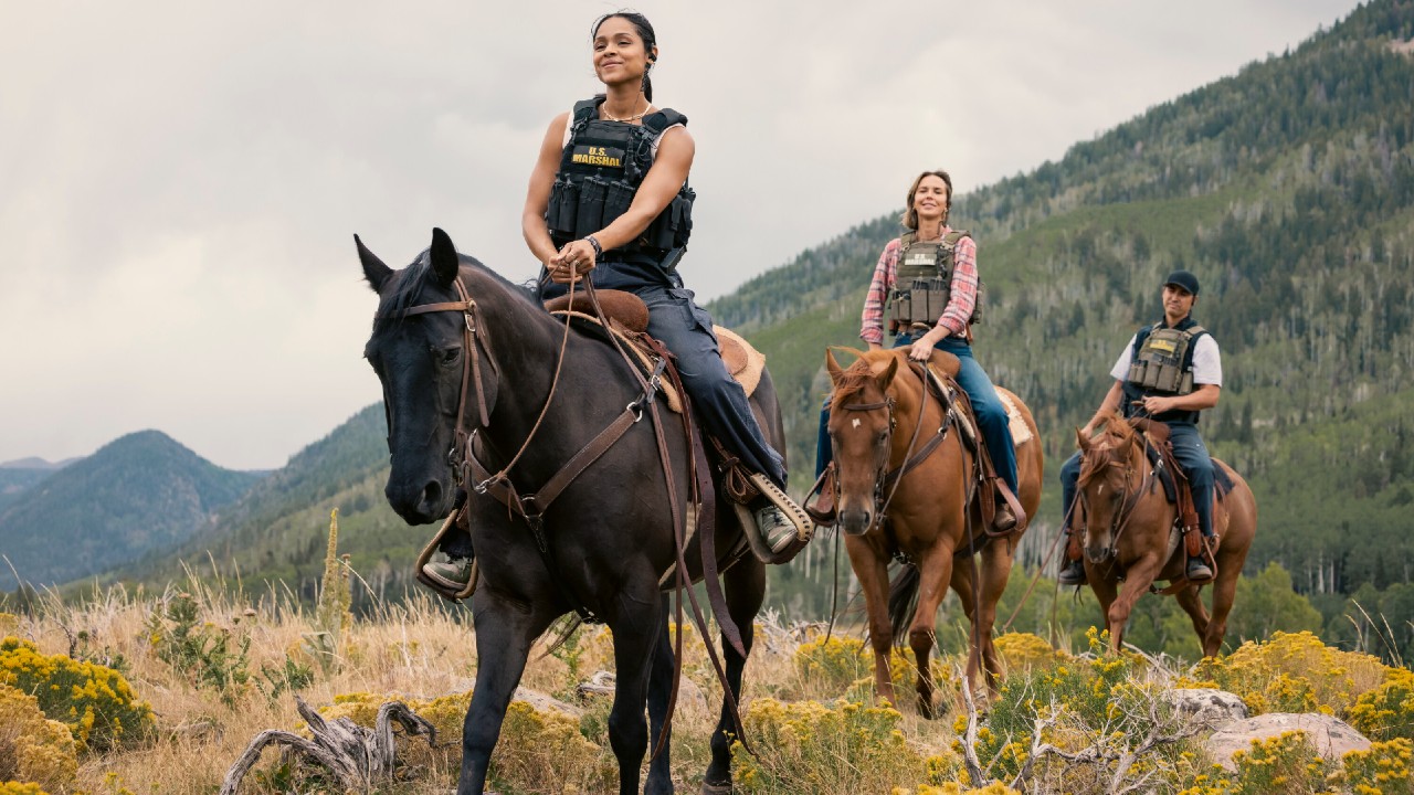 Pictured (L-R): Ash Santos as Andrea and Arielle Kebbel as Belle riding horses in a line.