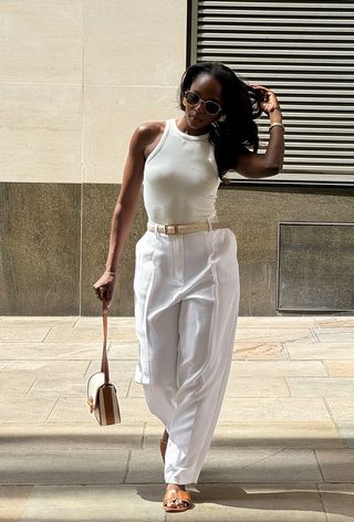 a photo showing what shoes to wear with wide-leg pants with a woman wearing a white tank top with a beige belt, white wide leg pants, and tan slide sandals