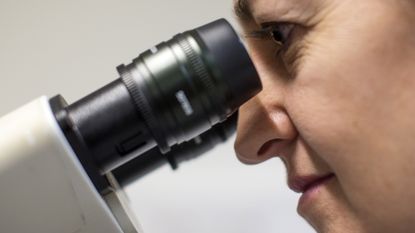 A scientist looks through a microscope, at Cancer Research UK Cambridge Institute