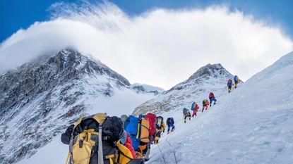 Roped team of mountaineers wearing backpacks and ascending snowy mountain slope