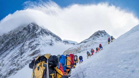 Roped team of mountaineers wearing backpacks and ascending snowy mountain slope