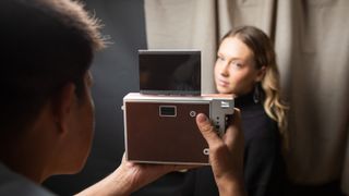 Someone holding a Lomo’Instant Wide Glass and taking a picture of someone with a curtain-like background behind