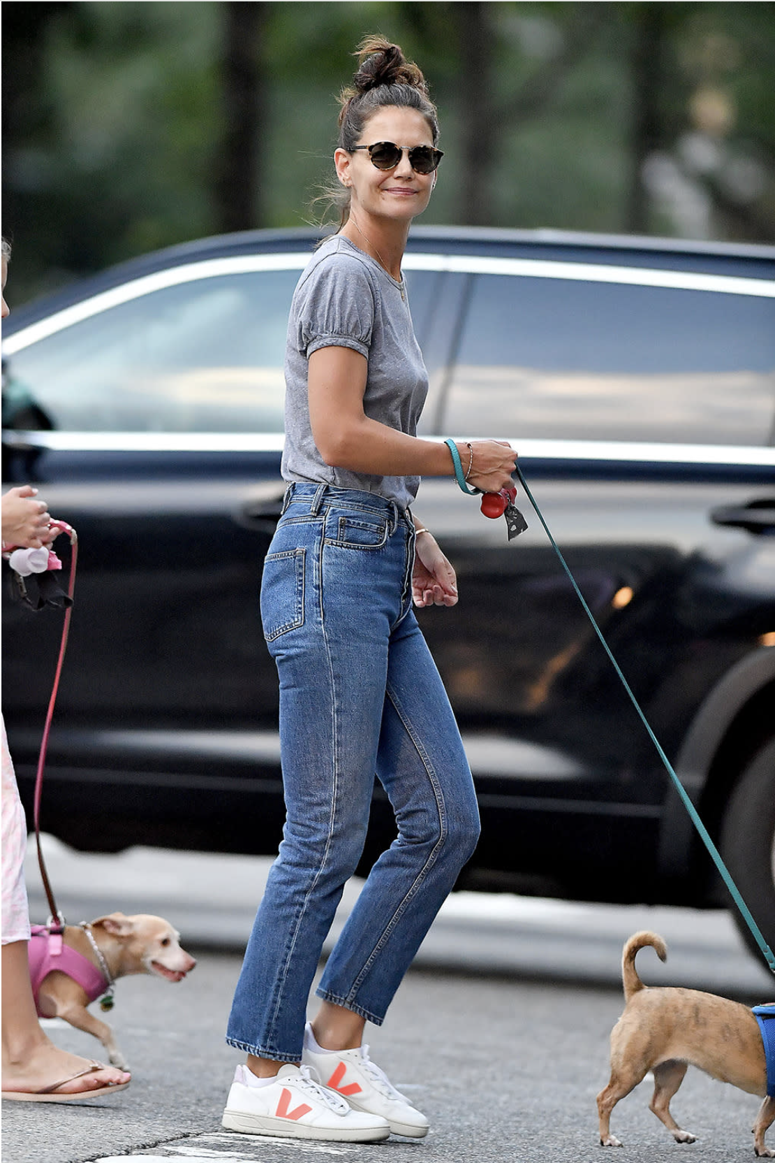 Katie Holmes wears a grey t-shirt a blue straight leg jeans and orange Veja trainer walking her dogs in Los Angles in a photo taken in 2023.