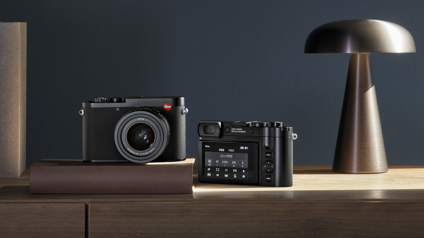 Two Leica Q3 cameras, one facing front and the other away, on wooden table