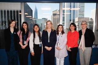 Duchess Sophie standing with a group of six women in front of a window showing the NYC skyline at a Plan International charity event