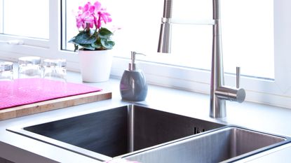 A kitchen sink with a window behind it and a dish drying rack next to it
