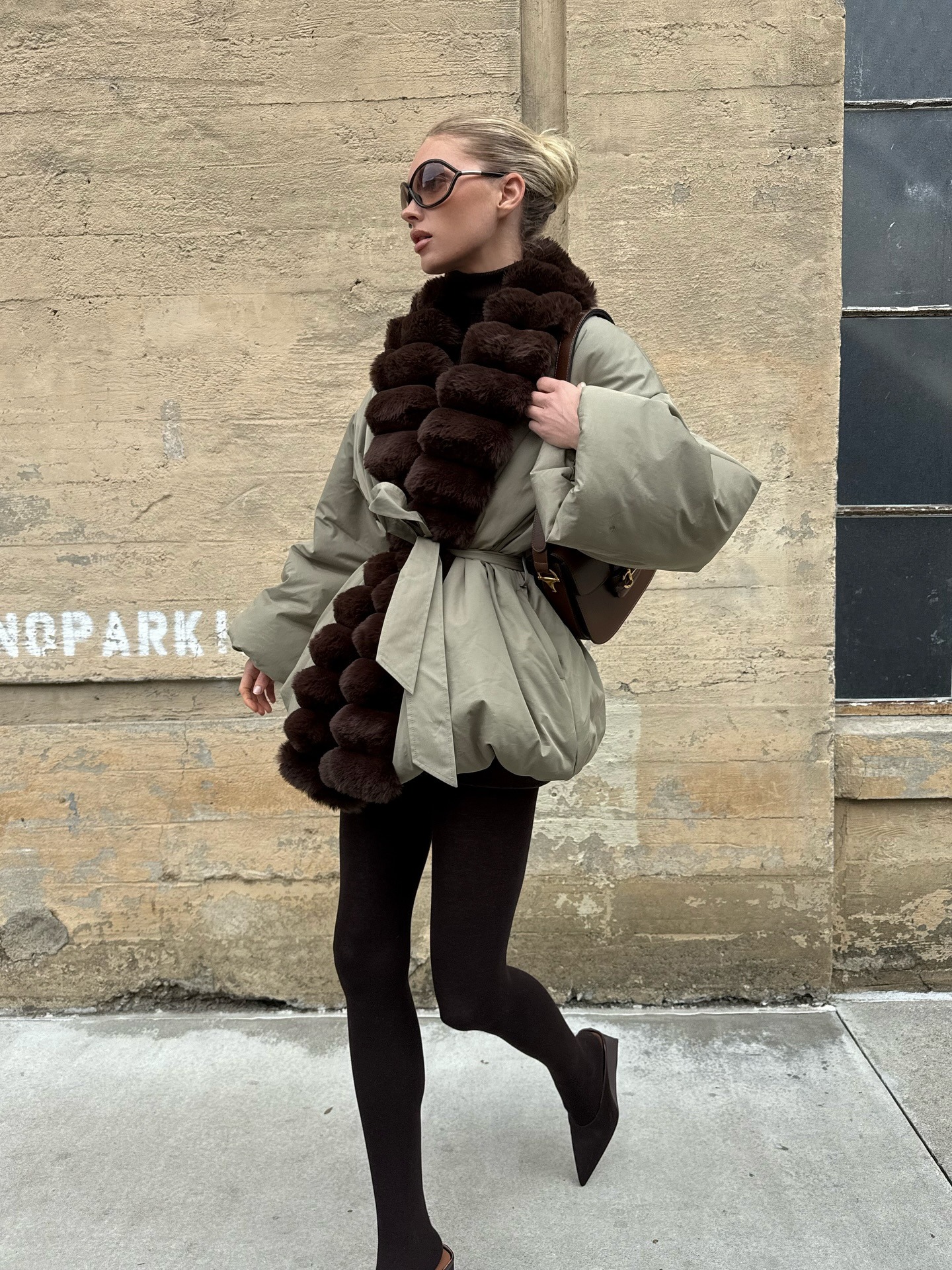 Elsa Hosk wearing a fur-trimmed parka, brown tights, and brown Alaia satin mules