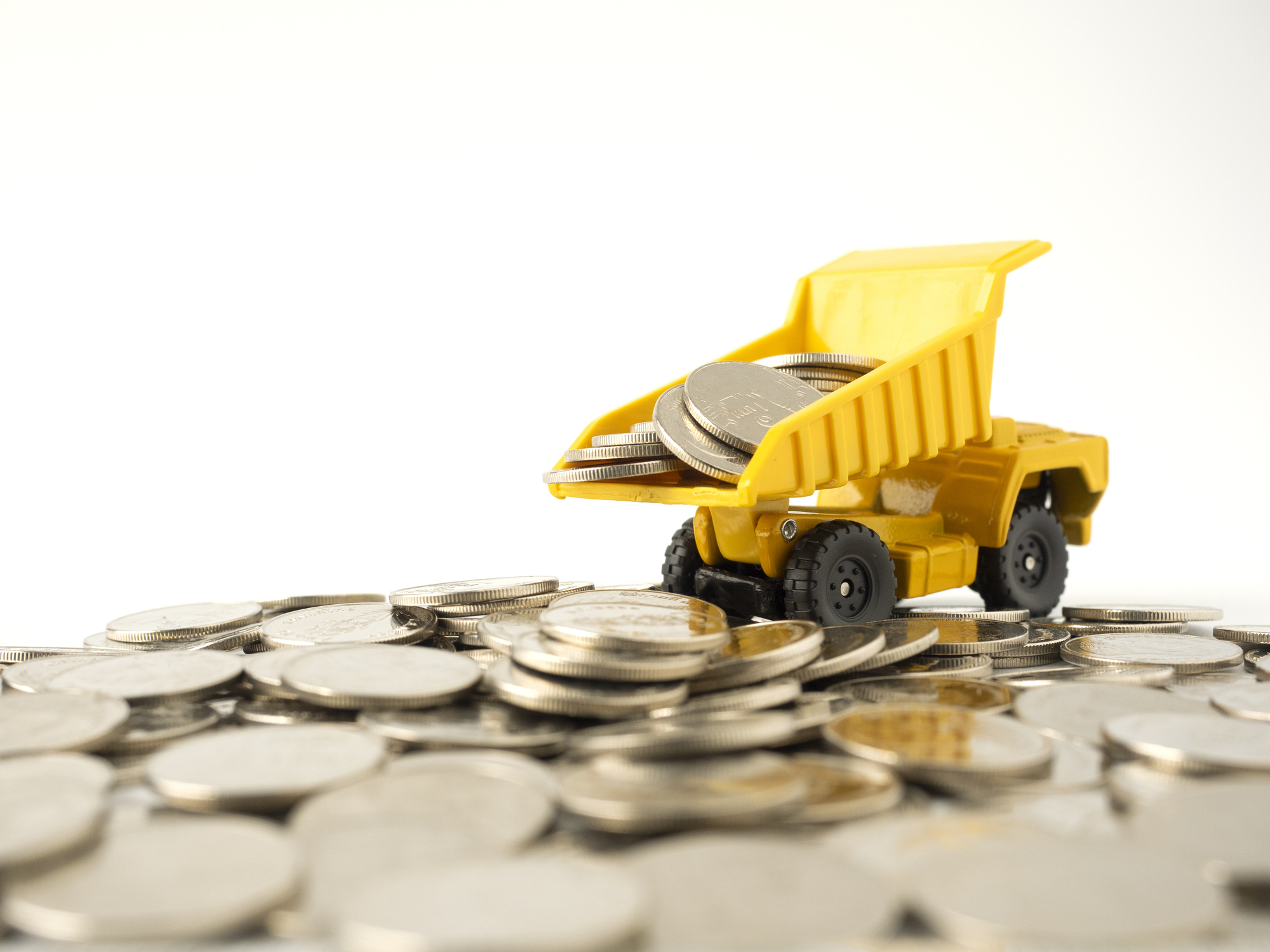 yellow toy dump truck unloading silver coins onto a white surface