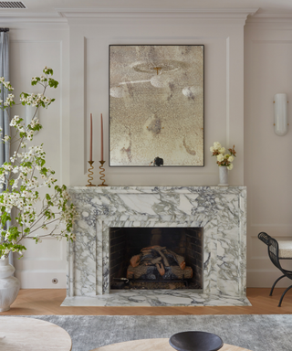 marble fireplace in living room with wooden floorboards and vase with blossom and wiggle candle sticks
