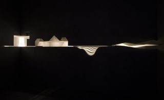 Light installation appearing to shine both upwards and downwards into geometrical objects in an otherwise black space