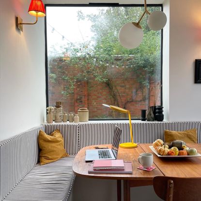 Banquette seating with striped cushions and an retro table with a yellow task lamp and laptop