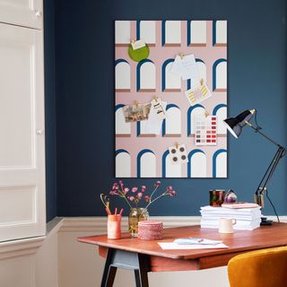 a desk and chair in a blue room beside a window with a large wallpapered pinboard on the wall