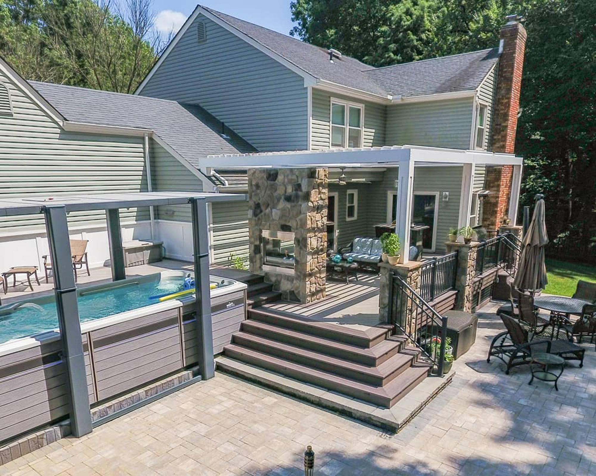 Swimming pool under deck with fireplace and grey decking