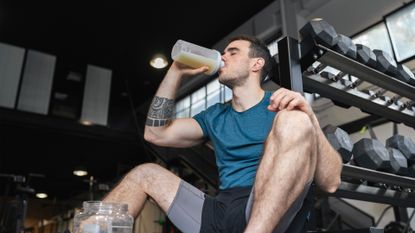 man drinking from a protein shaker at the gym
