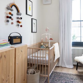 Neutral nursery with wooden cot and teddy, with overhanging mobile. Prints and rainbow art on wall