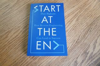 One of the best cycling books is this one in the image which is called Start at the End by Dan Bigham and is a blue cover on a wooden surface