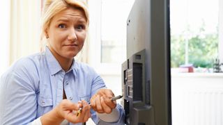 A woman holding two HDMI cables behind her TV, looking confused