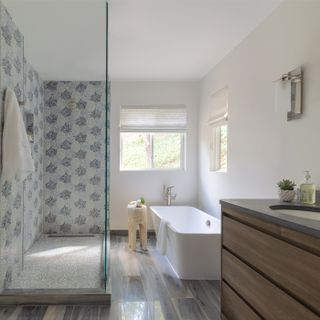 blue mosaic tiles in walk in shower, white tub, wooden floor, vanity