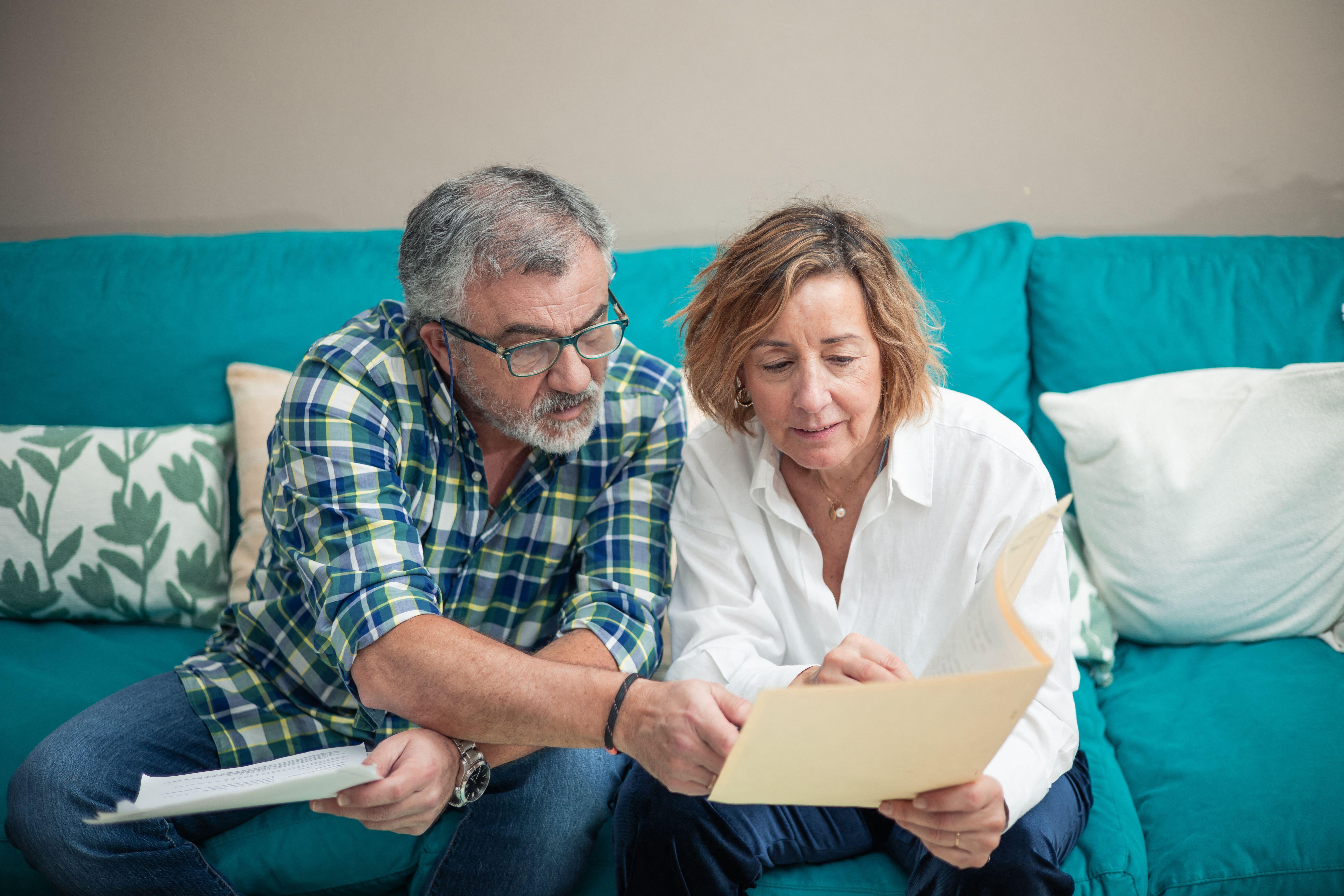 2WNY6PH a retired couple sits comfortably on their sofa, diligently sorting through papers and documents. One of them wears glasses, symbolizing focused atten