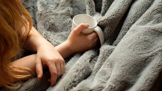 How heavy should a weighted blanket be? Person under a blanket with mug of drink