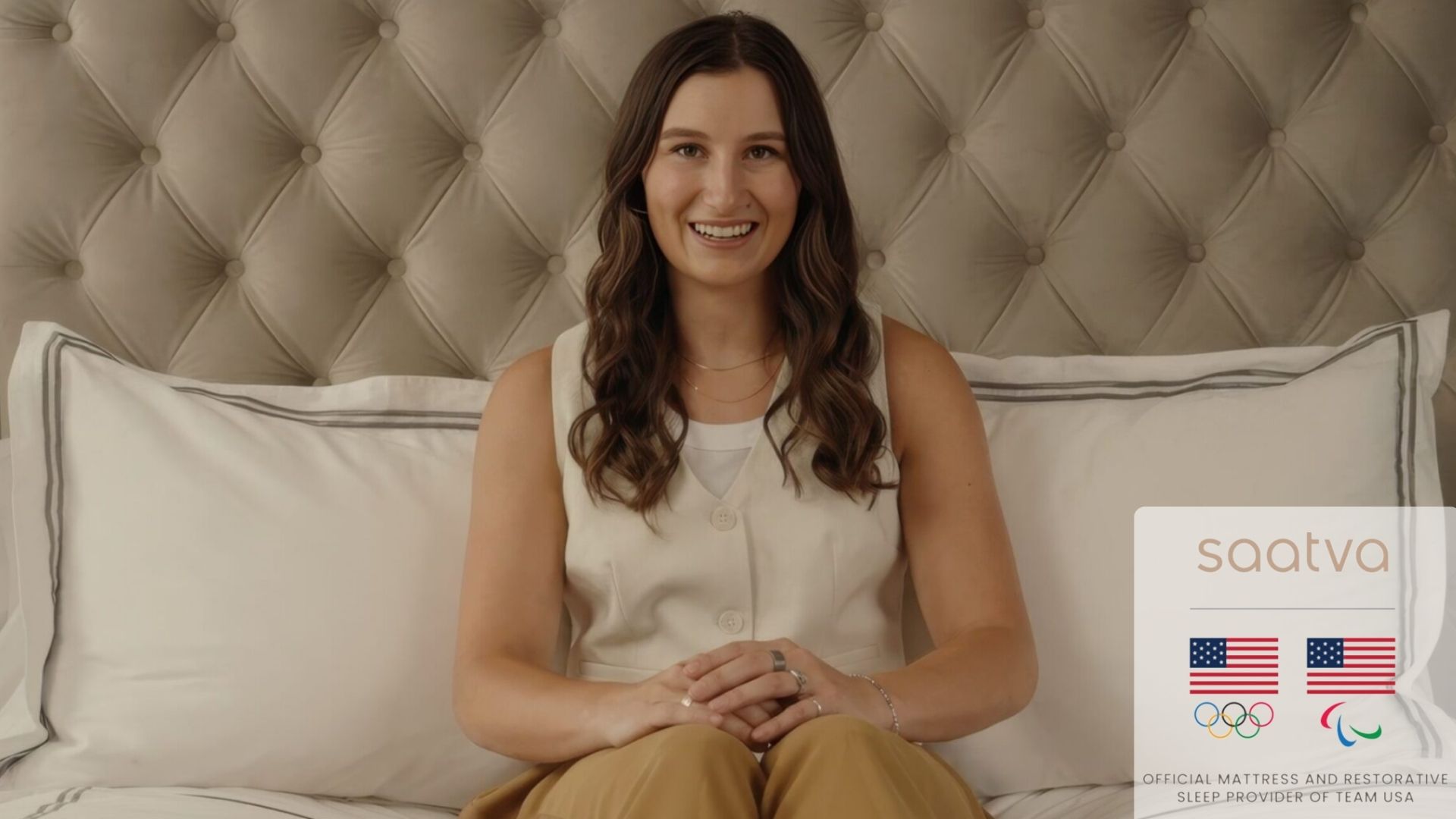 US skier Lauren Macuga sat on Saatva bed with a beige upholstered headboard and white pillows