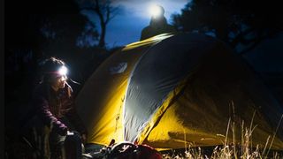 Man and woman pitching tent wearing Knog Bilby headlamps
