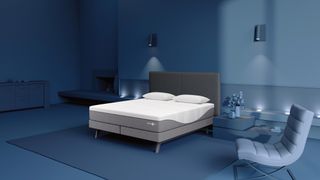 Grey and white Sleep Number i8 king size smart bed in a blue bedroom with blue walls, rug, chair and bedside shelving and two lamps on wall