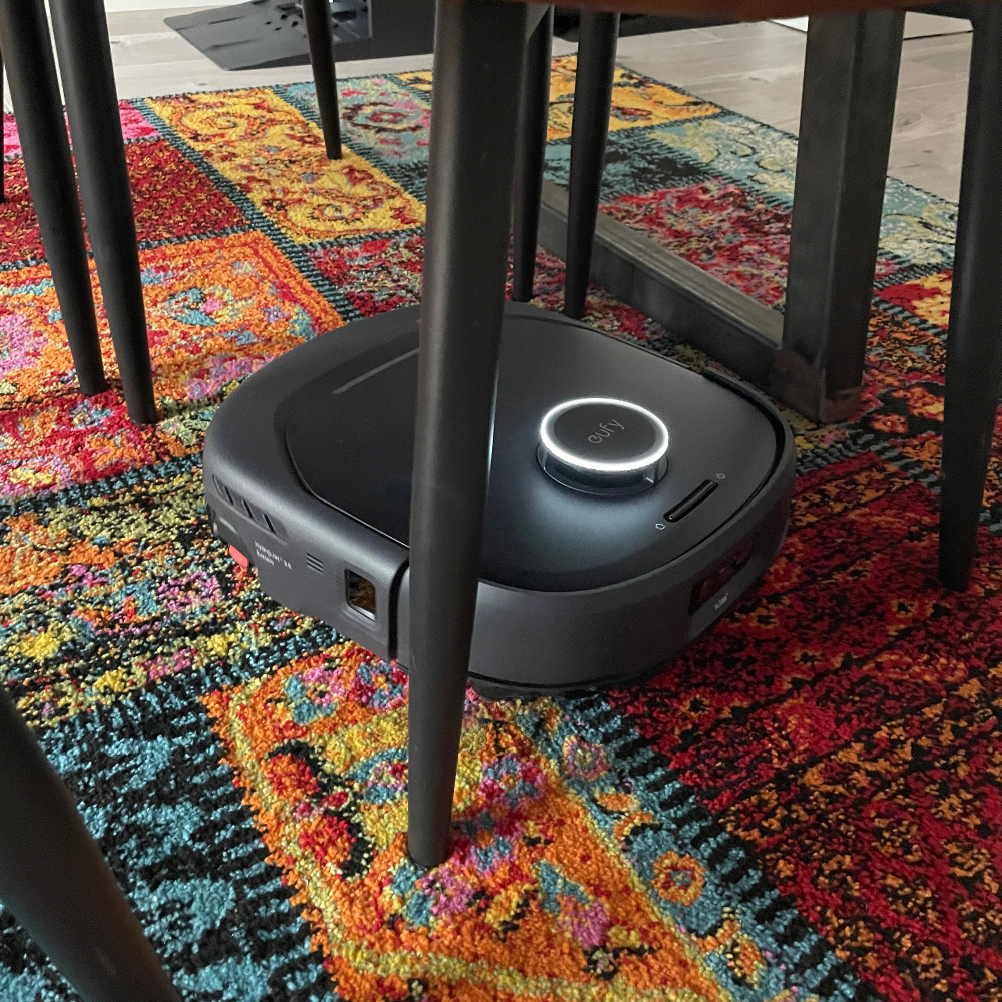 Anker eufy Robot Vacuum E35 Omni cleaning a colourful rug around dining room chairs