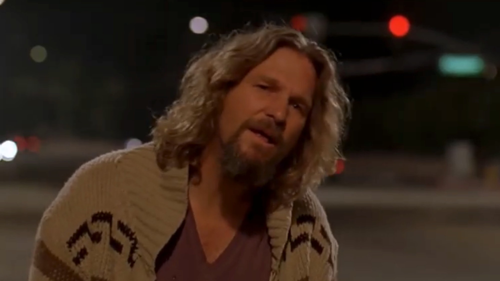 Jeff Bridges as the Dude, wearing a sweater and a purple t-shirt. looking stunned as his cab drives off in The Big Lebowski