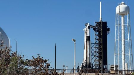 A black and white SpaceX Falcon 9 rocket stands atop a pad for Crew-10 under a clear blue sky