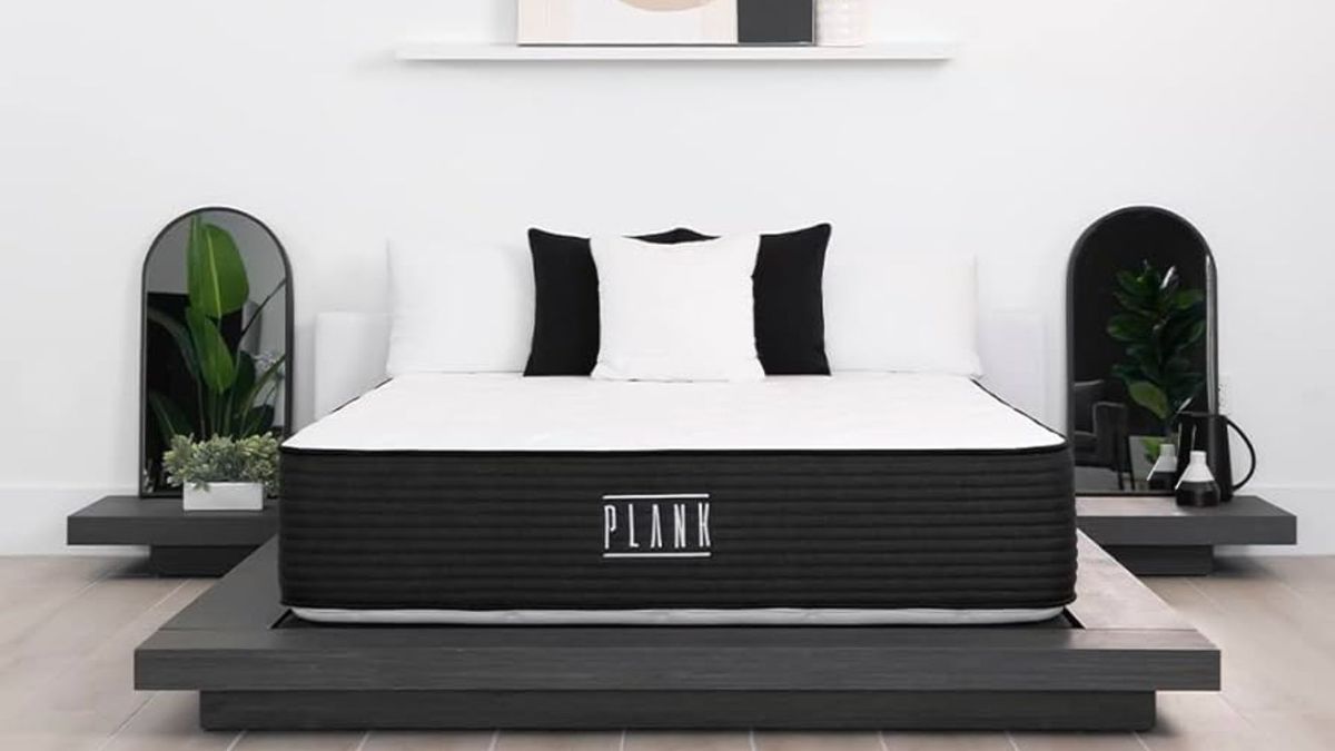 The image shows the Plank Firm mattress on a grey bed foundation in a neutrally decorated bedroom