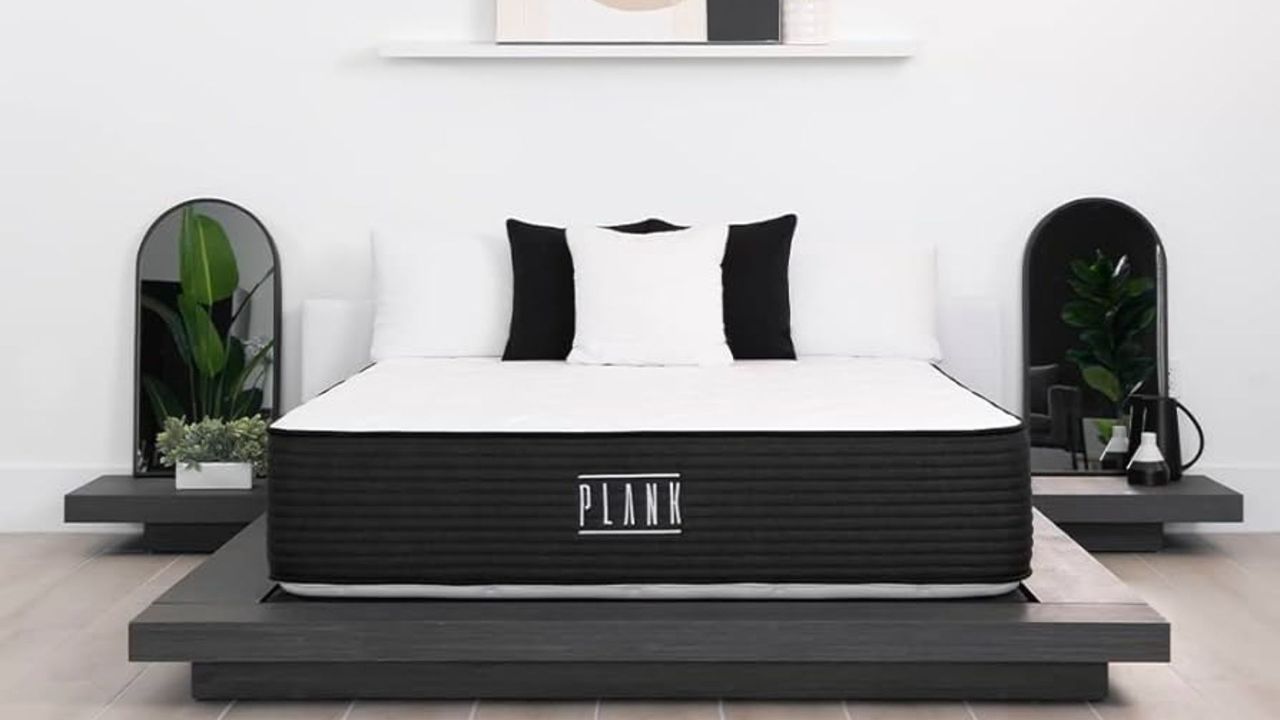 The image shows the Plank Firm mattress on a grey bed foundation in a neutrally decorated bedroom