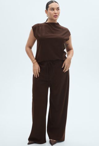 Model wears brown top and brown wide leg trousers with heels