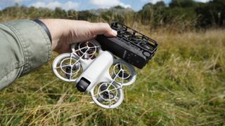 DJI Neo and HoverAir X1 held in a hand in a field