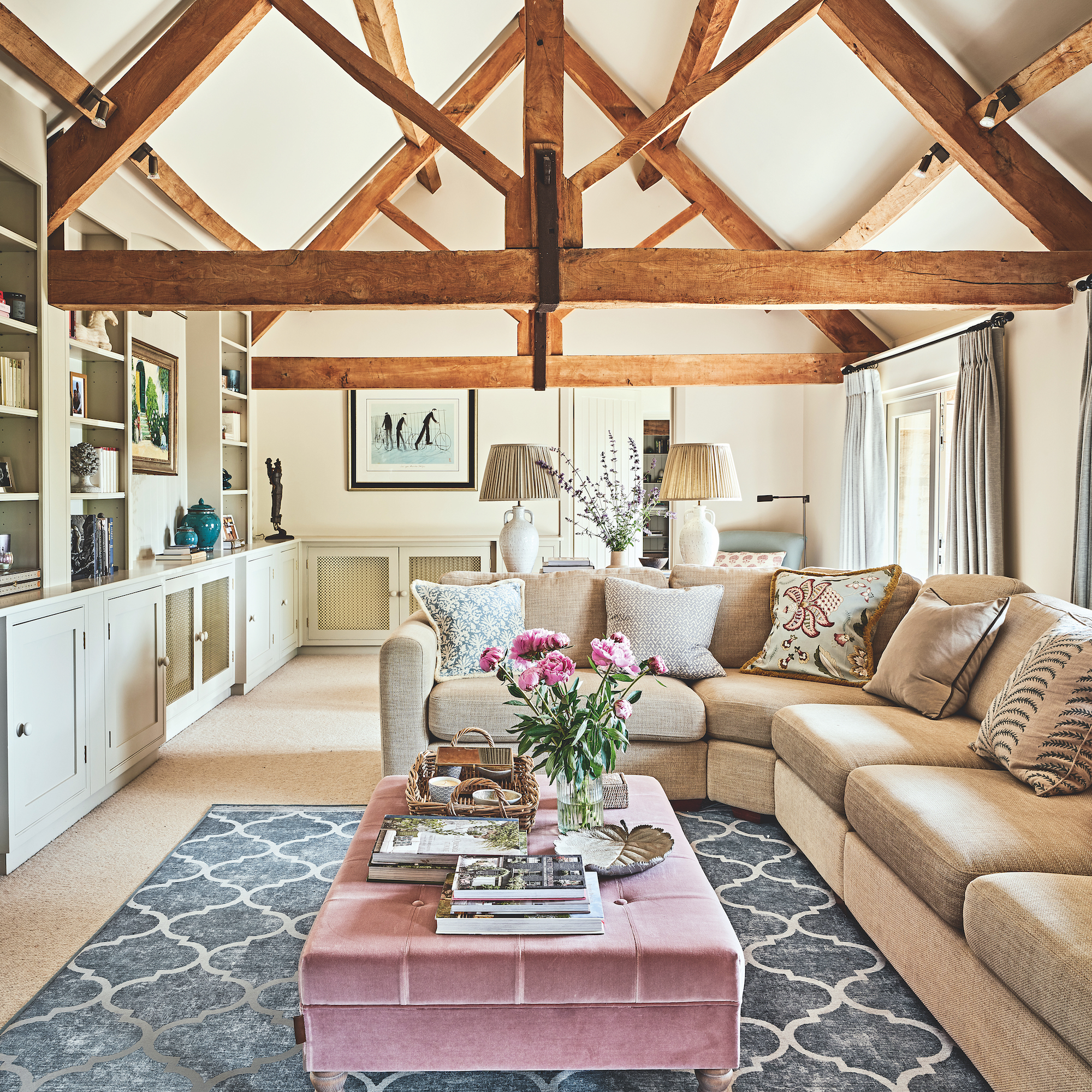 sitting room with vaulted beamed ceiling and pink ottoman coffee table with cream sofa and fitted cupboards