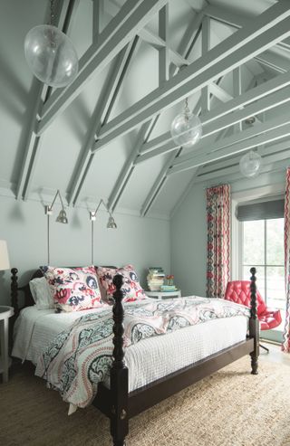 An attic bedroom with mint green wall paint decor, silver wall lights, red leather quilted chair, seagrass style carpet